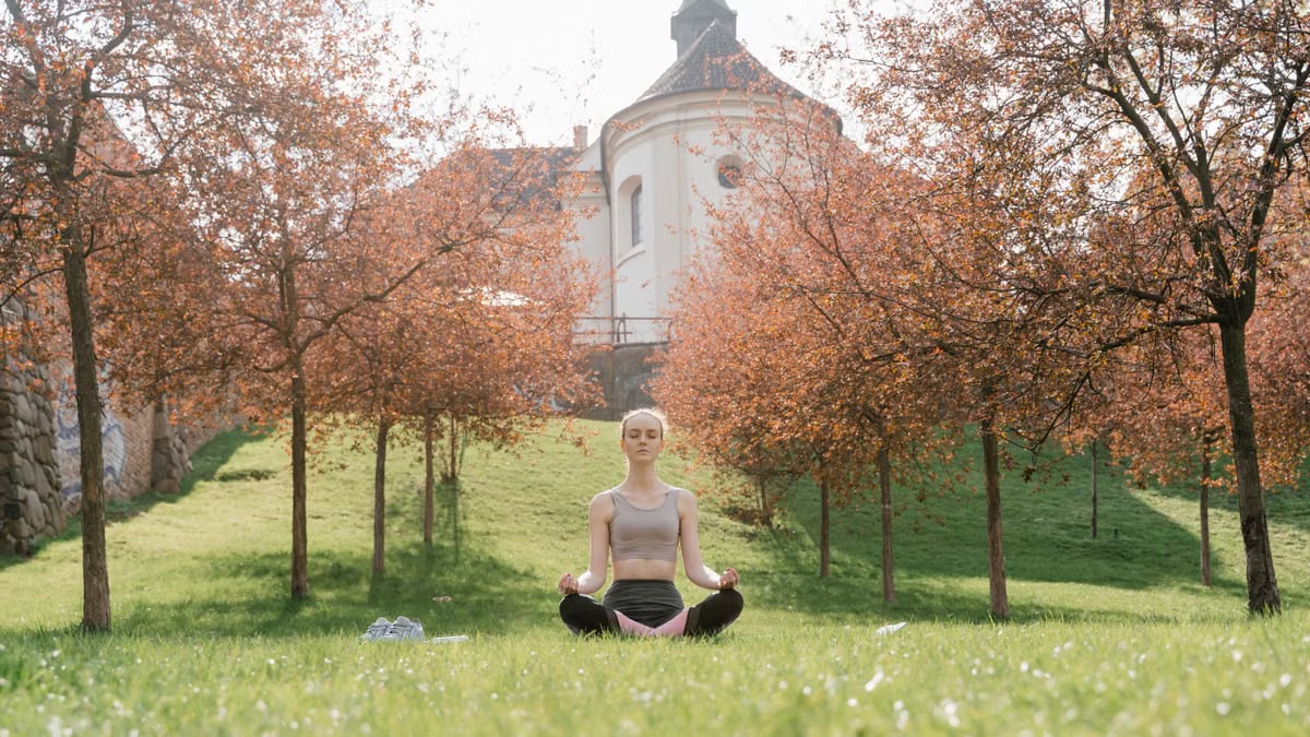 A woman practices meditation outdoors in a tranquil park during fall.