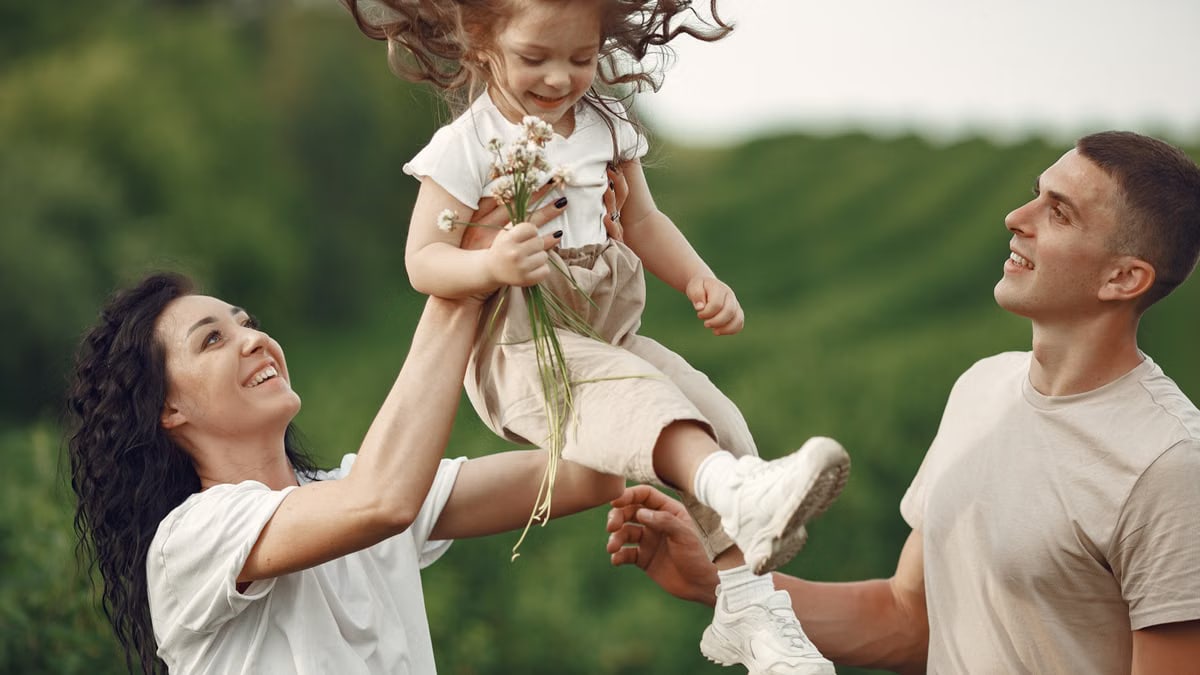 Happy family enjoying playful outdoor moment, lifting child in summer day.