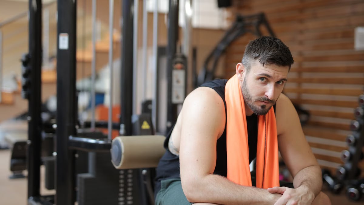 Adult male resting in a gym with an orange towel after strength training.